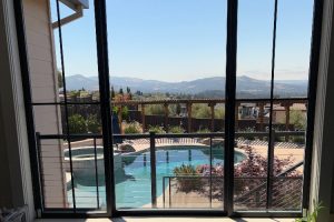 View from a glass-door interior looking out to a backyard pool, wooden deck, and distant mountains.