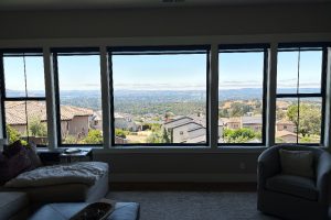 Living room with a row of large windows showing a suburban neighborhood and distant hills, bright and expansive.