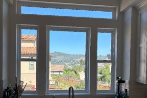 Bright kitchen with a large multi-pane window showing houses, greenery, and hills under a blue sky outside.