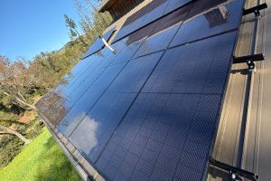 Solar panels tilted on a metal roof outdoors with a blue sky and trees in the background.