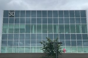 Glass office building with a grid of blue-tinted windows; '30' in the top-left corner and a tree in front.