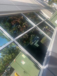 Commercial glass after cleaning - Transparent Window Washing Storefront with large glass windows reflecting trees and parked cars; gray frames and green exterior panels nearby.