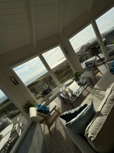 IMG_1317 - Transparent Window Washing Coastal living room with large windows overlooking the sea, white furniture, and a glass coffee table, plus a telescope by the window.