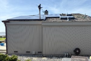 Two workers install dark solar panels on a residential roof under a blue sky.