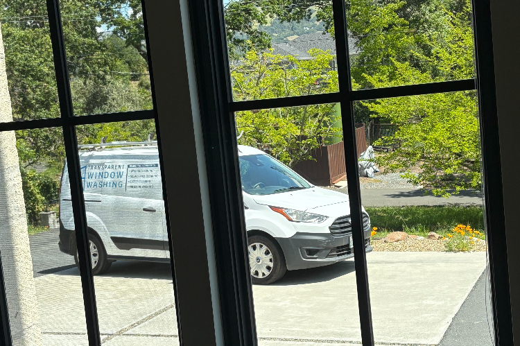 White van parked in a residential driveway, side panel reads 'Transparent Window Washing,' seen through a window.