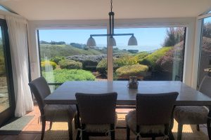 IMG_8170 - Transparent Window Washing Bright dining room with a rectangular table and six chairs, large glass walls open to a garden and ocean view outside.