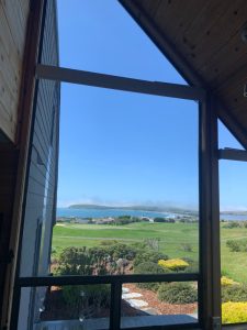 IMG_8302 - Transparent Window Washing Coastal view through a large wooden-framed window: blue sky, green lawn, houses, and the ocean beyond.